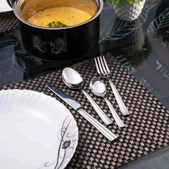 Stylish cutlery set placed on brown woven mat beside decorative plate and hot pot of dal.