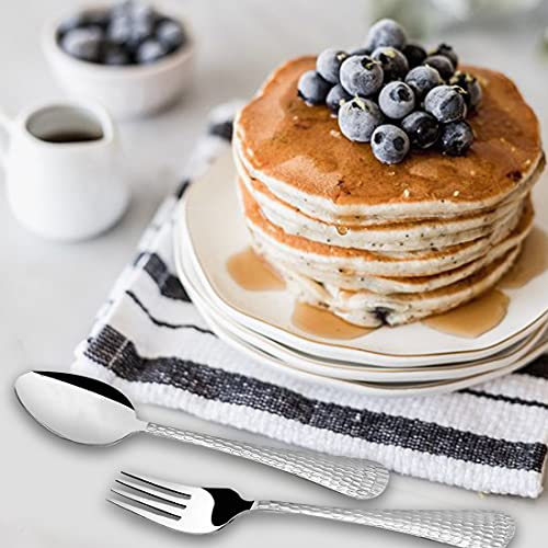 Fork and spoon with hammered handles placed beside stacked blueberry pancakes drizzled with syrup.