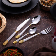 Elegant silverware with golden accents placed beside Indian dishes on a rustic brown dining table.