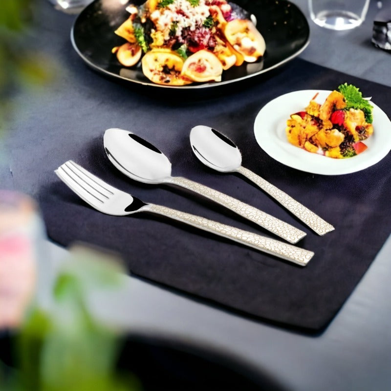 Three-piece cutlery set placed on black table with pasta dish and appetizer in stylish presentation.