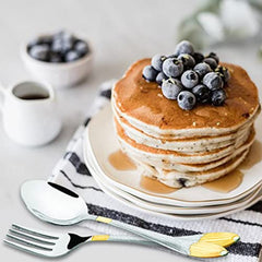 Stack of pancakes topped with blueberries and syrup, styled with elegant gold-silver cutlery beside plate.