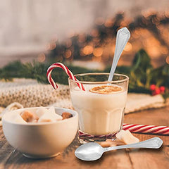 Decorative spoon in festive holiday drink with candy canes, cookies, and blurred lights in background.