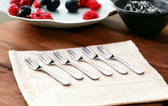 Six small forks arranged on white napkin with berries in background