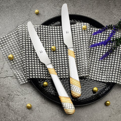 Elegant gold-accented knives on black plate with sparkling mesh mat and decorative golden beads.