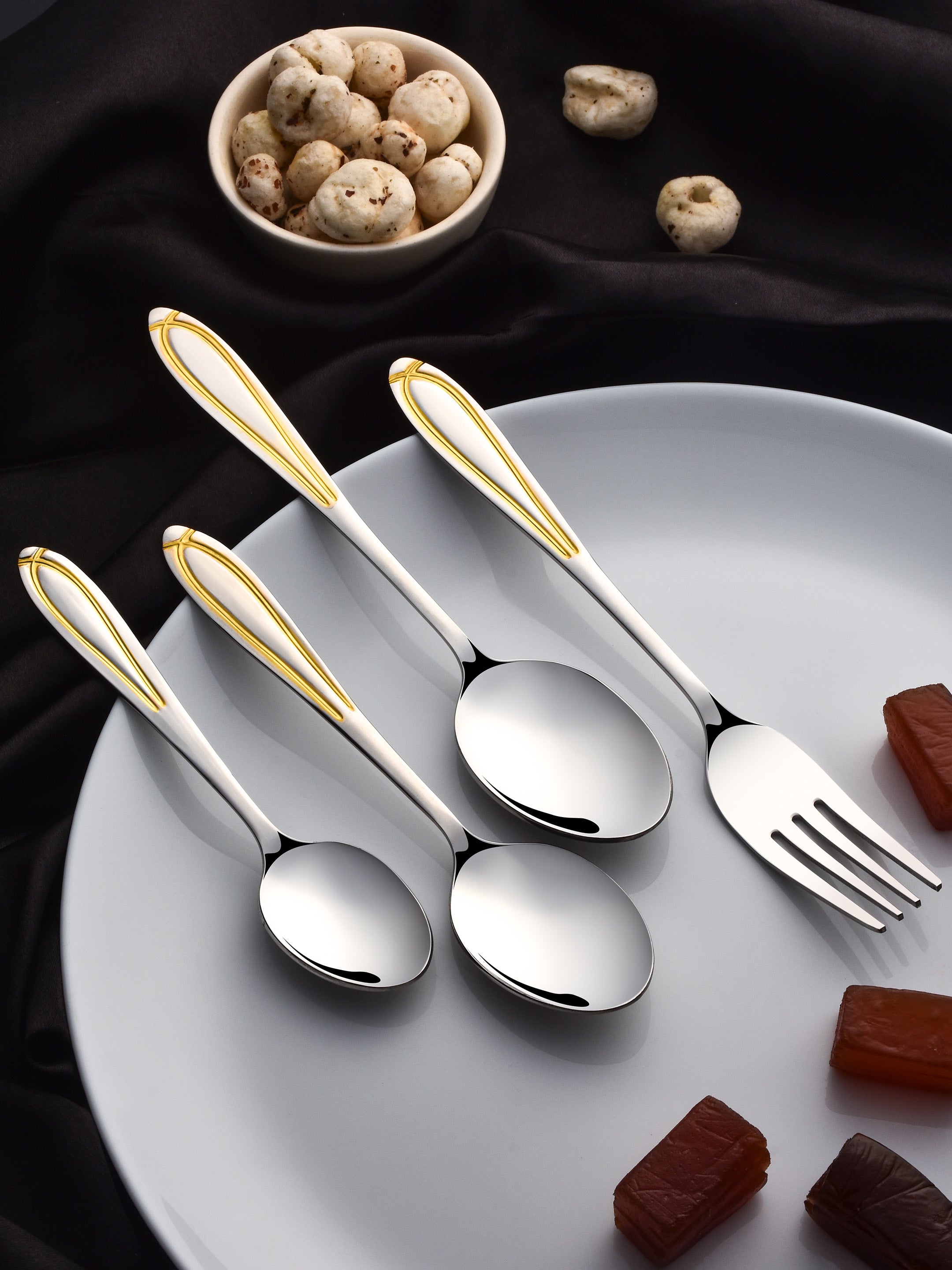 Four elegant stainless steel utensils with gold-plated handles on white plate, surrounded by mushrooms and chocolate pieces