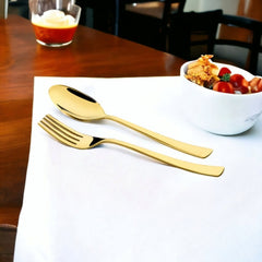Gold fork and spoon rest on white napkin beside a bowl of salad and dessert.