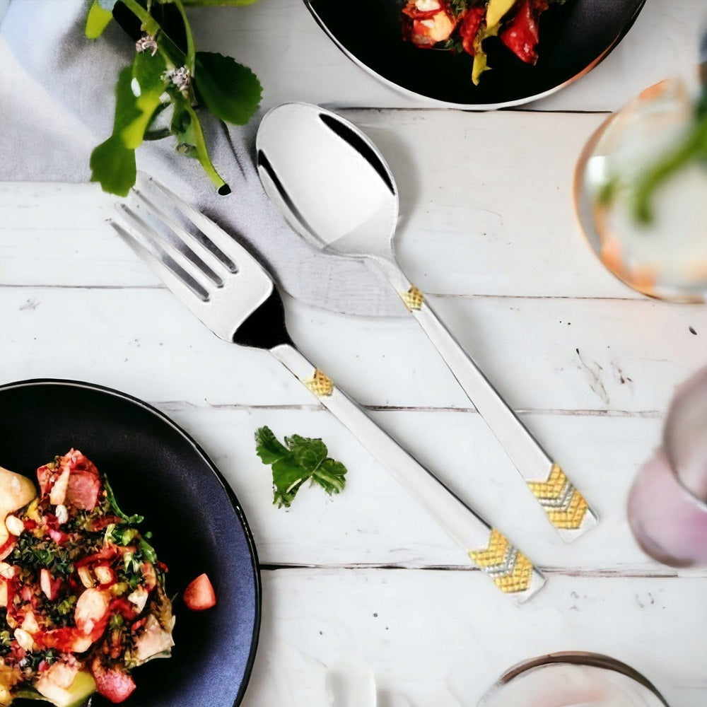 Elegant silver spoon and fork with gold accents styled beside plates of colorful gourmet food.