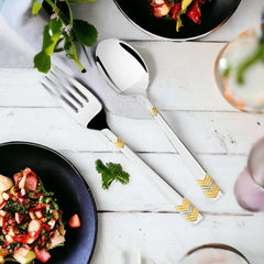 Elegant silver spoon and fork with gold accents styled beside plates of colorful gourmet food.