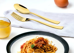 Elegant gold cutlery placed on napkin next to plate of spaghetti and glass of juice.