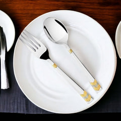 Silver spoon and fork with gold detailing placed neatly on a white ceramic dinner plate.
