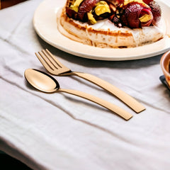 Gold spoon and fork resting on white cloth near a dessert plate with fruit and cream.