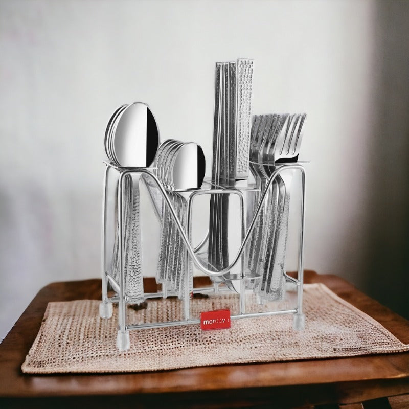 Complete stainless steel cutlery set in stand, placed on wooden table with woven beige mat.