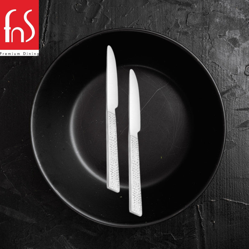 Two FnS Helios stainless steel knives with modern perforated handles arranged on black round plate in dramatic monochrome styling.