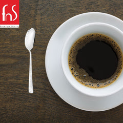 Helios teaspoon placed beside white coffee cup and saucer on wooden table, showcasing elegant mirror finish and textured handle in lifestyle setting.