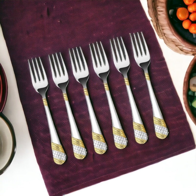 Six ornate stainless steel forks with gold and silver decorative handles on purple napkin