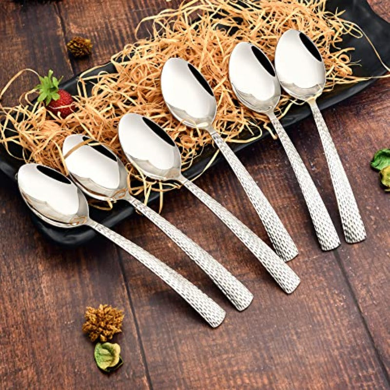 FNS Madrid 6 piece baby spoon set with hammered textured handles arranged on rustic wooden surface with black plate and decorative straw