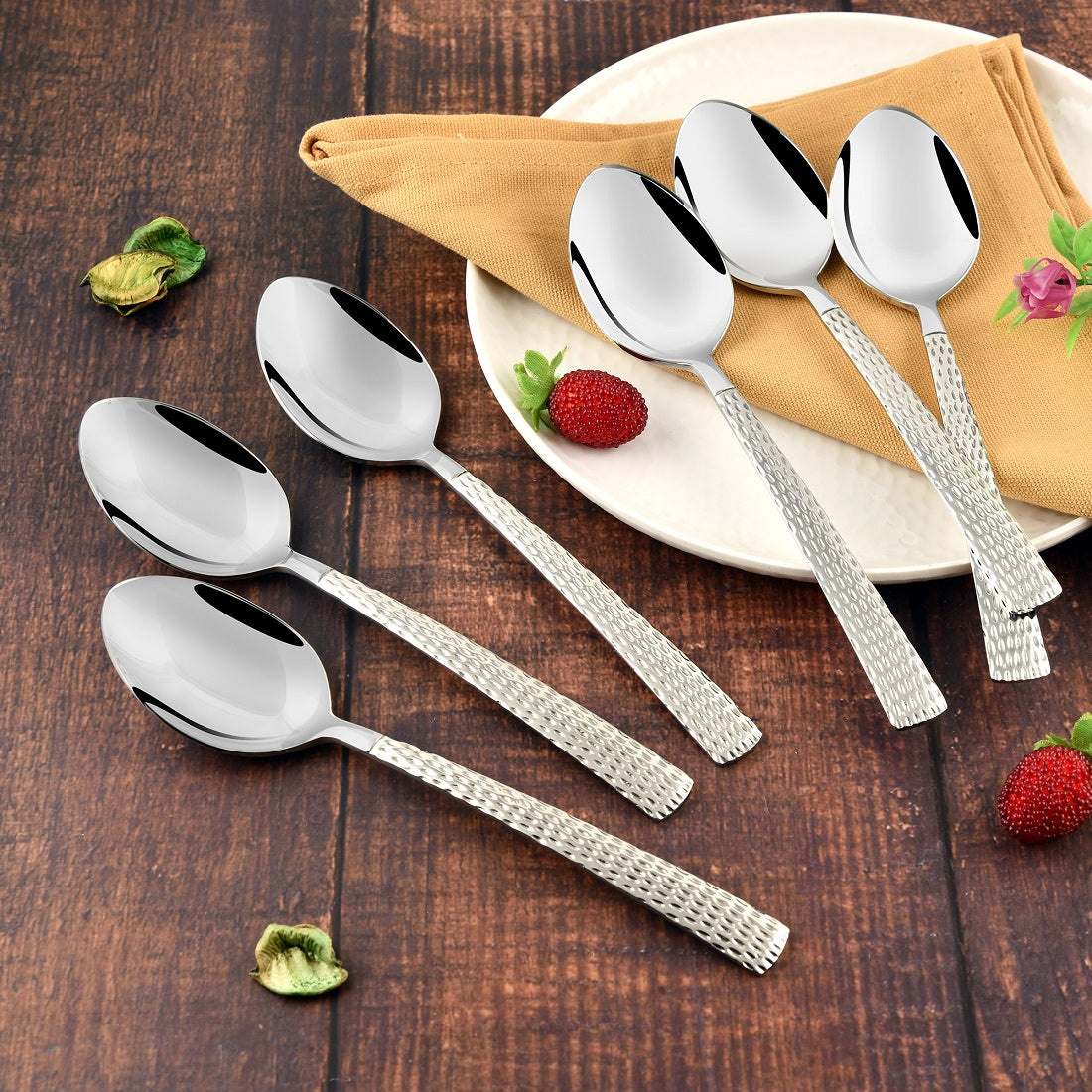 Six FnS Premium Dining stainless steel spoons with textured handles arranged on rustic wooden table with white plate, beige napkin, and fresh strawberries as decorative styling