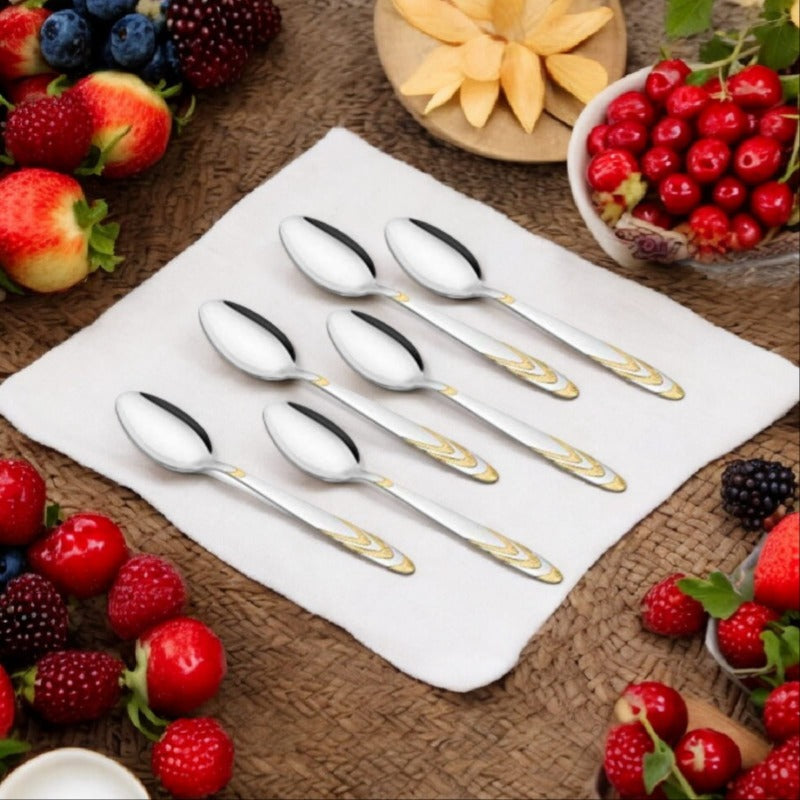 Six stainless steel teaspoons with gold-accented handles arranged on white napkin, surrounded by fresh strawberries, cherries, blackberries, and sliced apples on woven placemat.