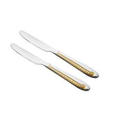 Two polished stainless steel dinner knives with luxurious gold-plated ornamental handles featuring intricate pattern detail, arranged diagonally on white background.