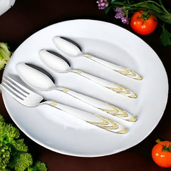 Elegant gold-accented fork and spoons arranged on white dinner plate, surrounded by vegetables and garnish.