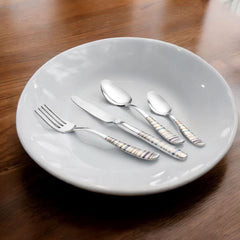 Navia cutlery set of four utensils with textured handles artfully arranged on white ceramic plate with wooden table and ambient indoor lighting.