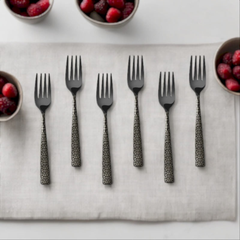 A set of six dinner forks with black heads and geometric patterned handles arranged on a white cloth, surrounded by bowls of berries.