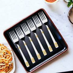 Six silver forks with gold accents in black presentation box near pasta