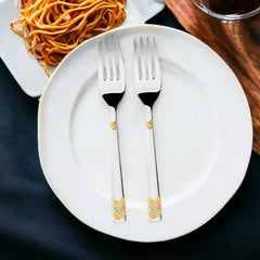 Two silver forks with gold accents on white plate beside pasta bowlRetry