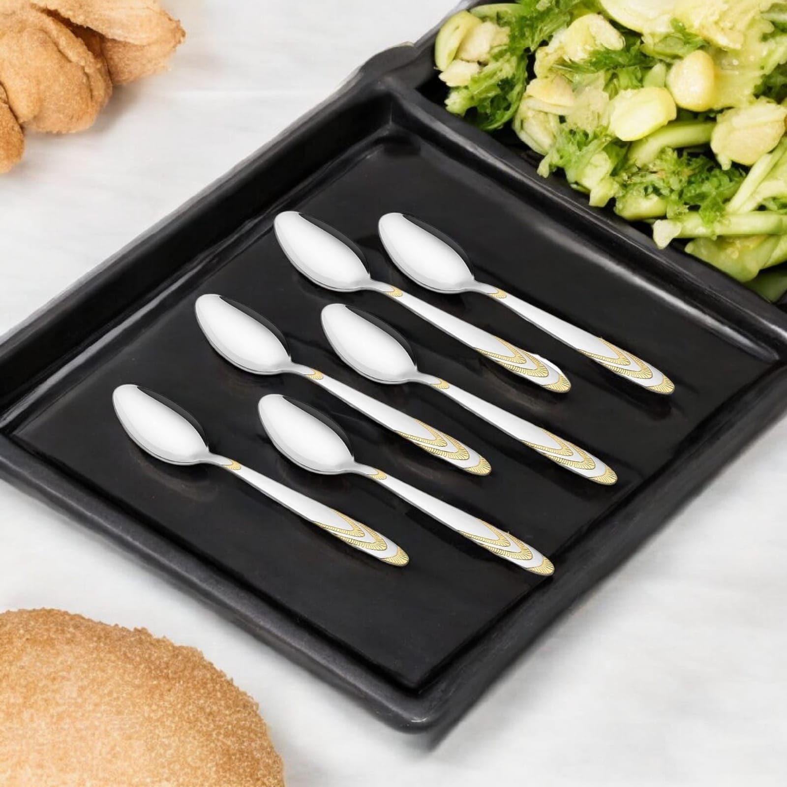 FNS 6-piece spoon set with gold accent handles arranged on black serving tray next to fresh cucumber salad