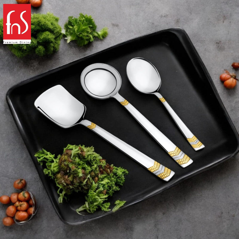 FNS Raga 3-piece gold accent serving utensil set arranged on black rectangular tray with fresh greens and cherry tomatoes lifestyle table setting