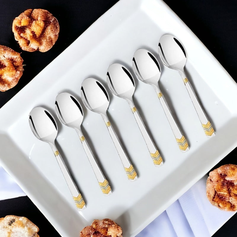 FNS Raga 6-piece baby spoon set with 24-karat gold plated handles displayed on white plate with pastries, elegant infant feeding cutlery.