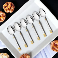 FNS Raga 6-piece baby spoon set with 24-karat gold plated handles displayed on white plate with pastries, elegant infant feeding cutlery.