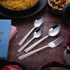 Fork and three spoons with textured handles placed beside noodles, books, and snacks on rustic table.