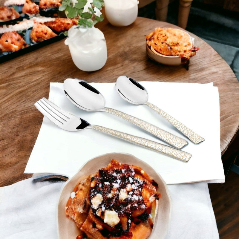 Fork and two spoons with elegant handles resting on white napkin beside lasagna and baked dishes.
