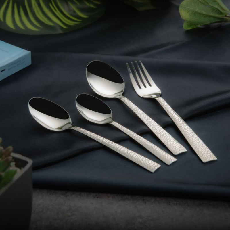 Stylish cutlery set featuring engraved silver handles displayed on dark blue fabric with plants around.