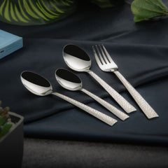 Stylish cutlery set featuring engraved silver handles displayed on dark blue fabric with plants around.