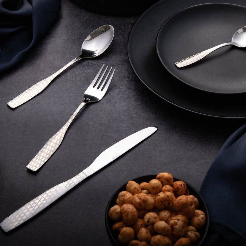 Elegant silver cutlery beside black dinnerware and seasoned makhana, arranged on a dark slate surface.