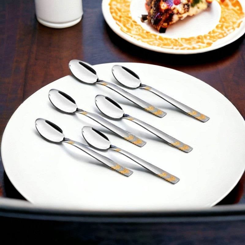 Six-piece FNS Raga gold plated baby spoon set arranged on white plate in elegant dining setting, premium feeding utensils for infants and toddlers.