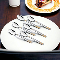 Six-piece FNS Raga gold plated baby spoon set arranged on white plate in elegant dining setting, premium feeding utensils for infants and toddlers.