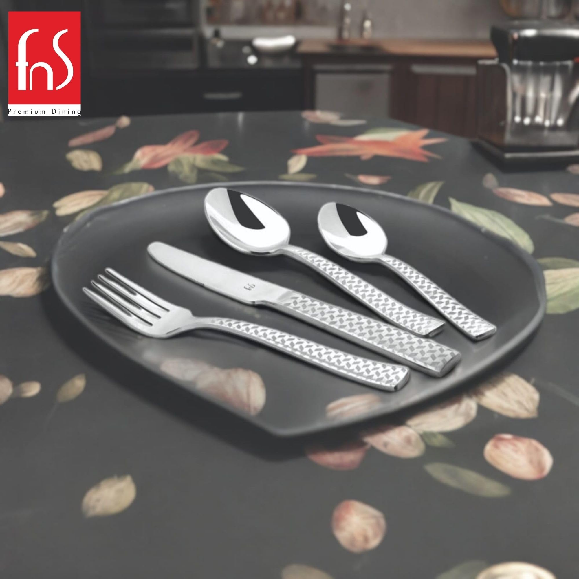 Fork, knife, spoon, and teaspoon with diamond-textured handles placed on black plate with floral tablecloth.