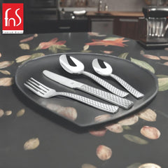 Fork, knife, spoon, and teaspoon with diamond-textured handles placed on black plate with floral tablecloth.