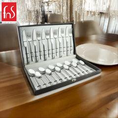 Elegant boxed stainless steel cutlery set with patterned handles displayed on a wooden dining table.