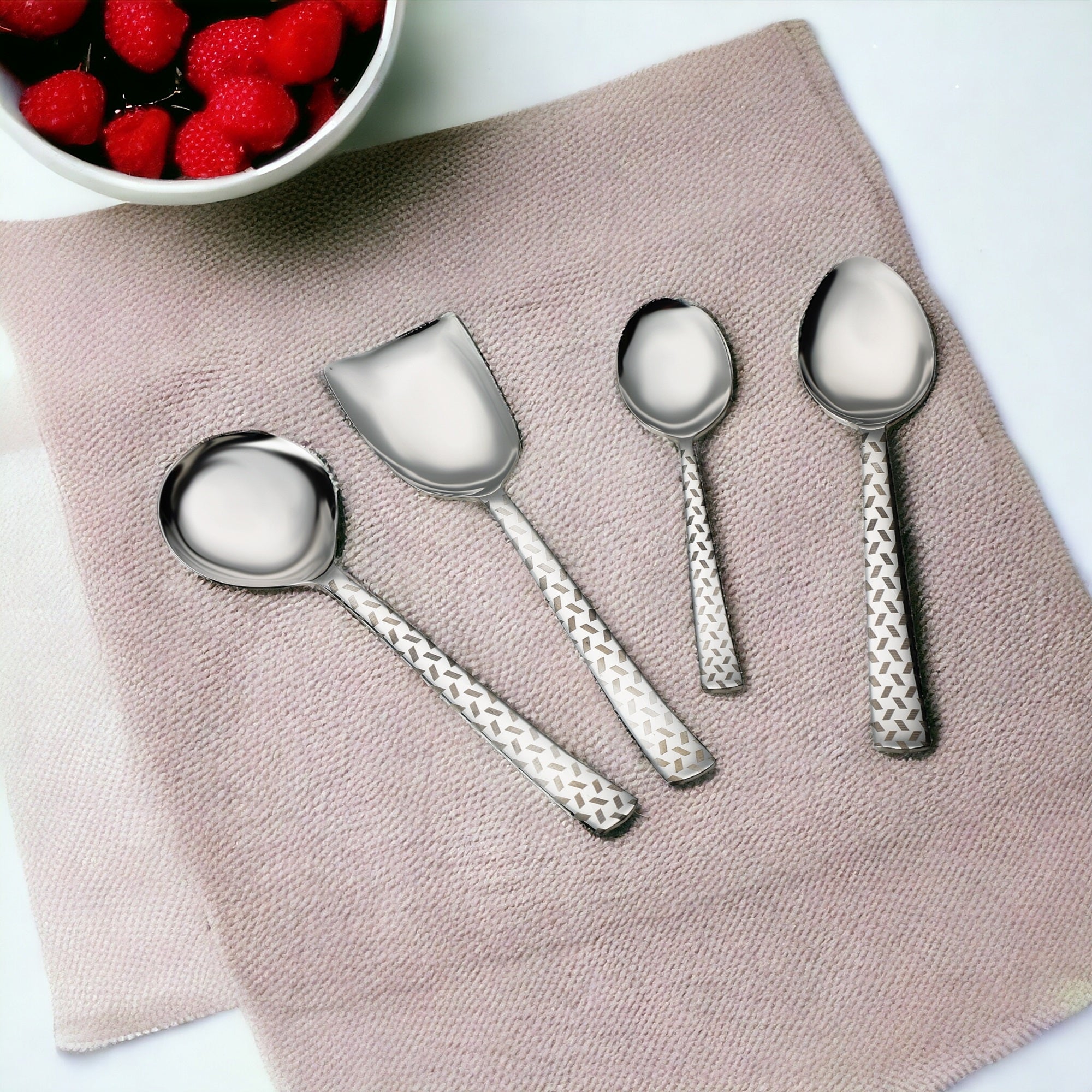 FNS Rhombo stainless steel 4-piece serving set arranged on pink linen placemat with bowl of fresh strawberries for elegant table setting