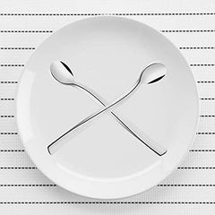 Two FNS Slim Line long drink spoons crossed on white plate displaying elegant curved design and mirror finish, modern minimalist beverage cutlery collection.