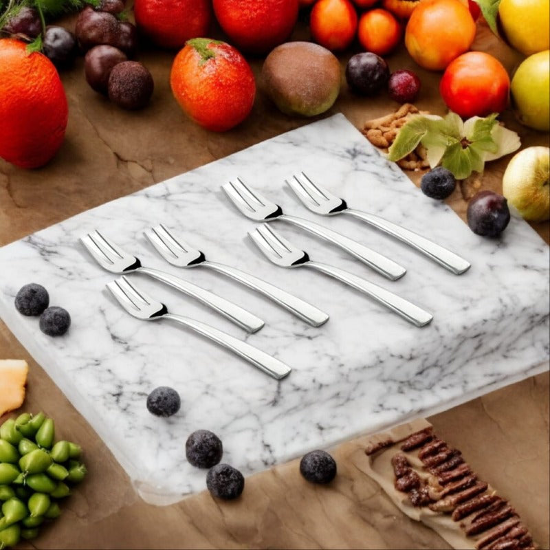 Six silver fruit forks arranged on marble board surrounded by fresh fruits