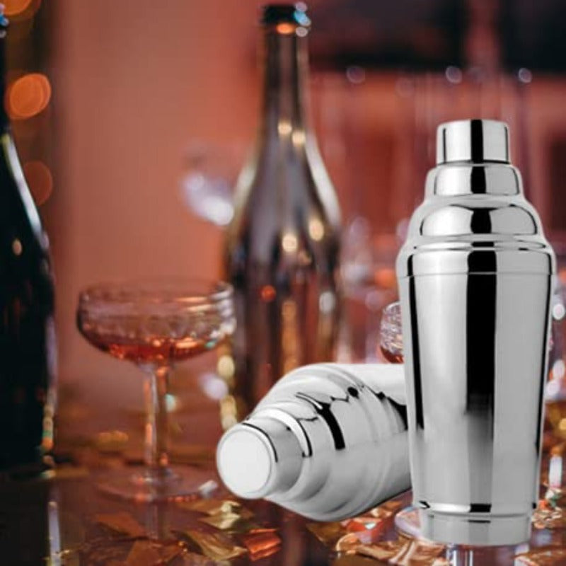 FNS stainless steel cocktail shakers displayed on bar with champagne bottles, coupe glasses, and warm bokeh party lighting