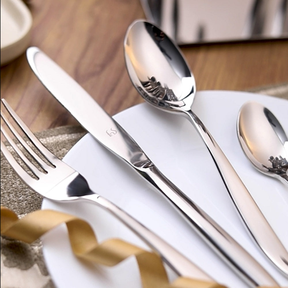 Polished cutlery set on white plate with decorative ribbon and wooden table background, elegant presentation.