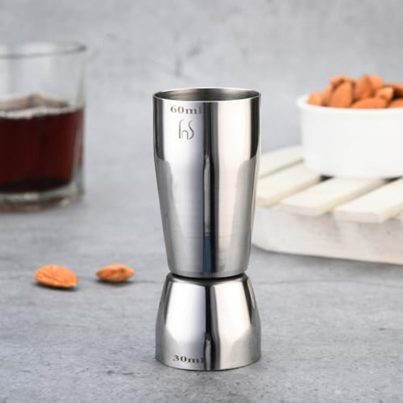 FNS stainless steel dual jigger peg measure 60ml/30ml on grey counter with cocktail, almonds, and bar accessories
