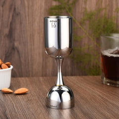 FNS stainless steel double jigger with 60ml and 30ml markings on wooden table with white bowl of almonds and dark beverage glass