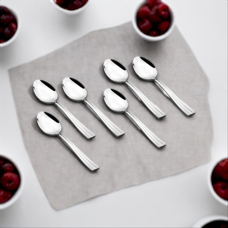 FNS Venice 6 piece stainless steel baby spoon set with sleek tapered handles arranged on grey napkin surrounded by fresh berries in white bowls